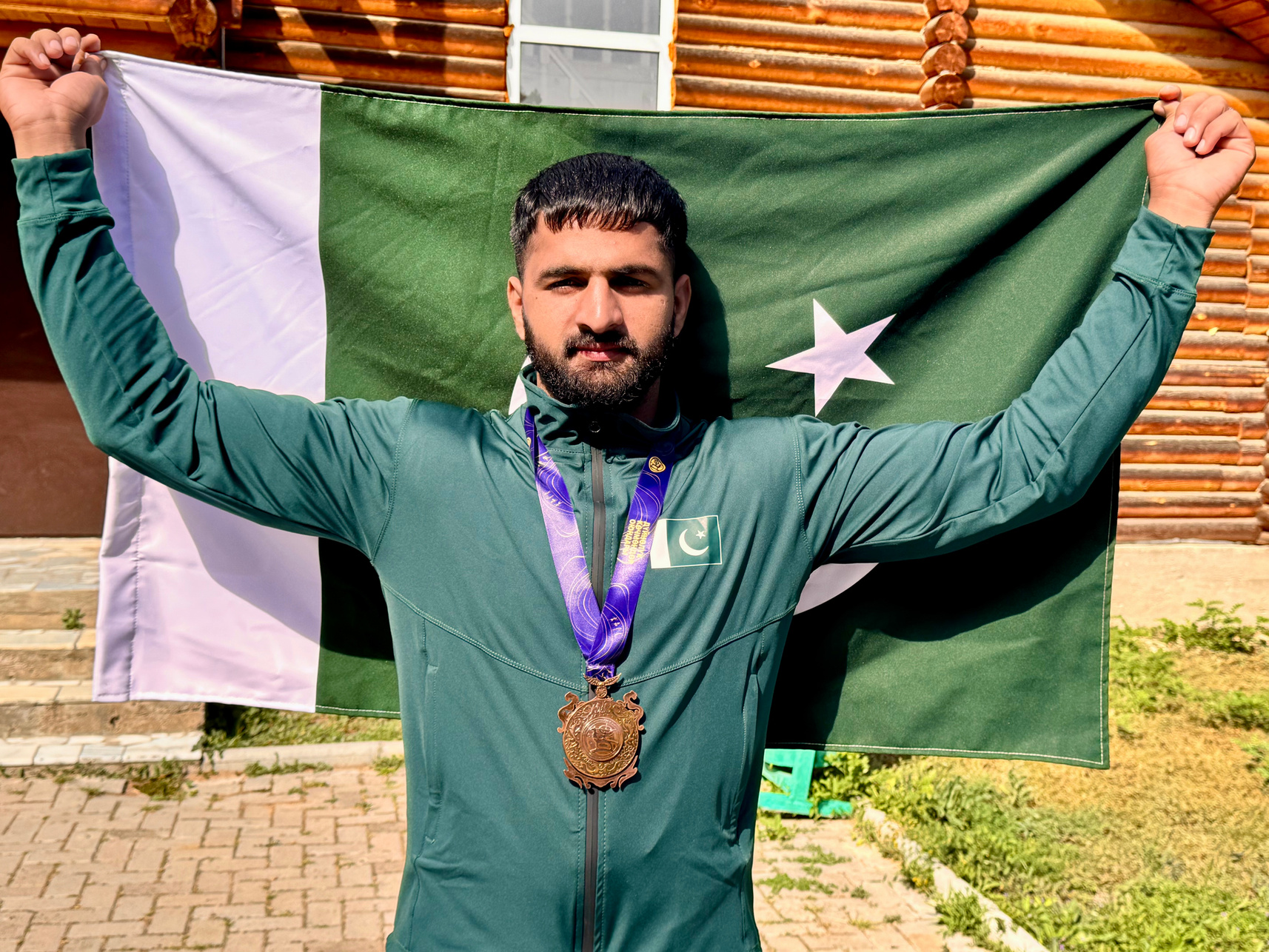 Muhammad Asim celebrating with the Pakistan flag and bronze medal